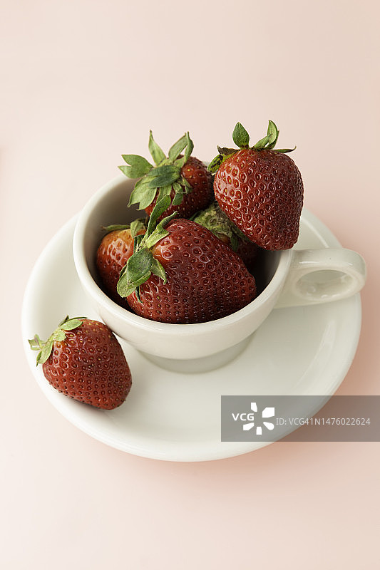 粉色背景上装满新鲜草莓的白色杯子图片素材