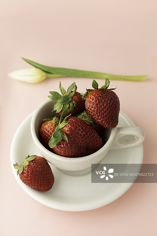 粉色背景上的草莓杯和白色郁金香图片素材