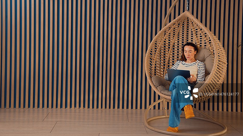 女人坐在舒适的悬挂式秋千椅上用笔记本电脑工作图片素材