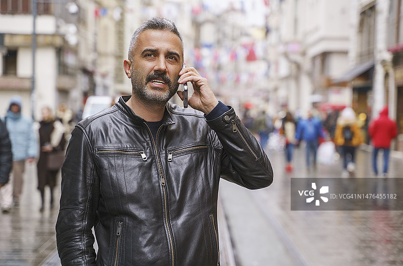 在土耳其伊斯坦布尔街头用手机交谈的皮夹克男人图片素材