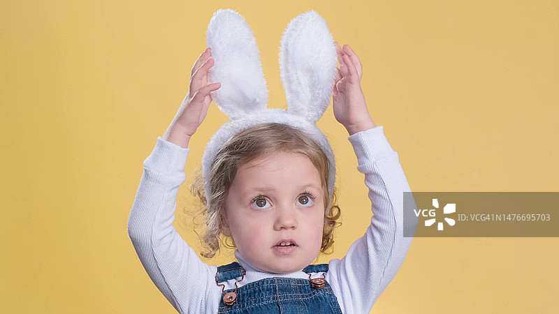 在黄色背景上戴着兔子耳朵的快乐小女孩图片素材