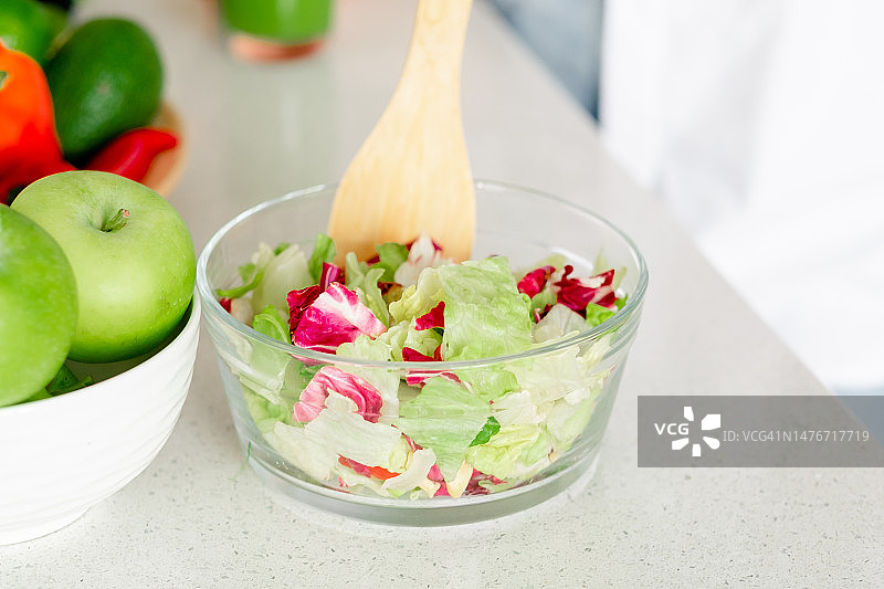 厨房桌子上透明碗里的卷心菜和蔬菜沙拉，旁边是青苹果图片素材