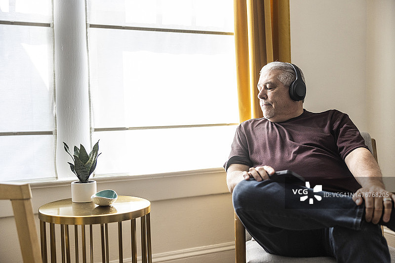 戴着无线耳机，望着窗外的年长男人图片素材