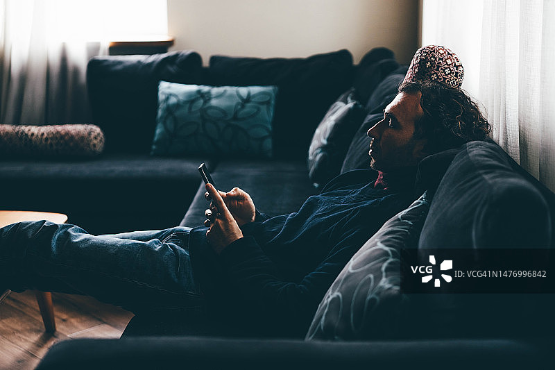 男子躺在沙发上用智能手机浏览社交媒体图片素材