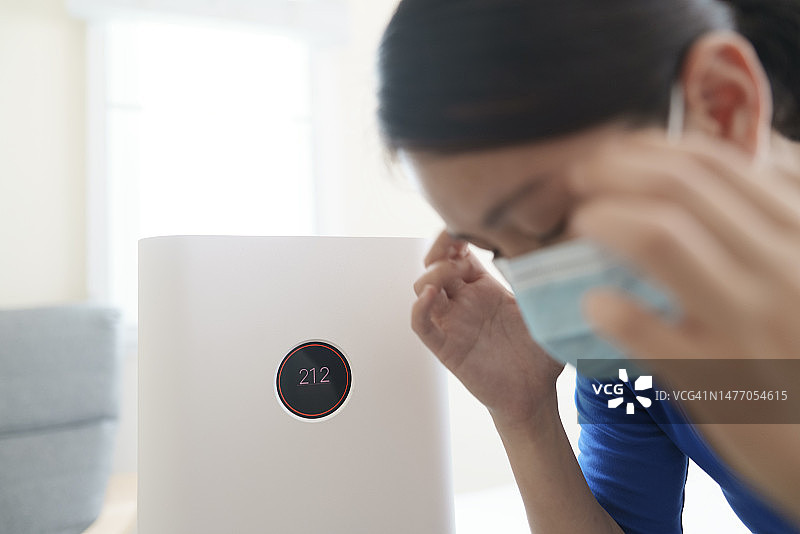 空气污染下的负面情绪：佩戴N95口罩的亚洲女性在卧室拥抱空气净化器（泰国清迈）图片素材