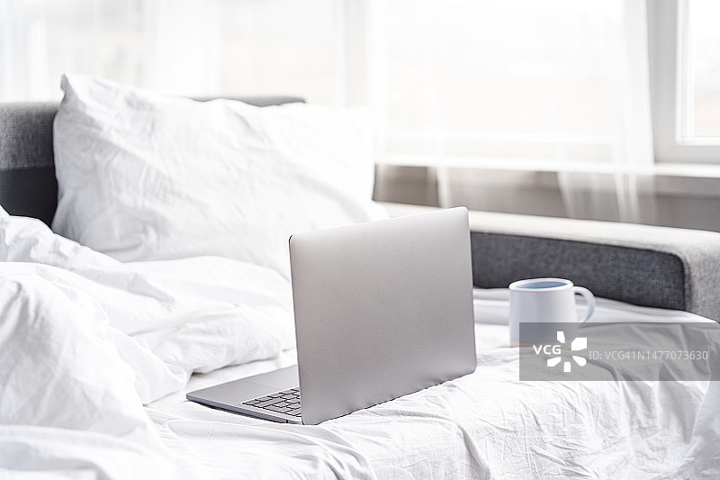 清晨，铺着白色床单的床上放着一台打开的笔记本电脑图片素材