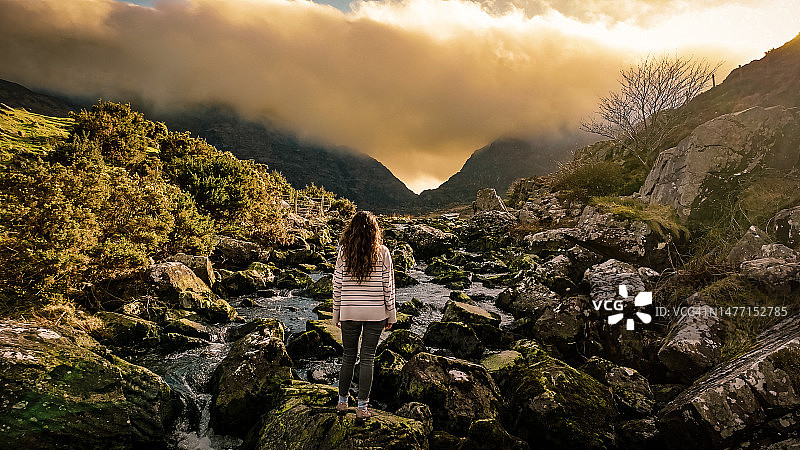 爱尔兰凯里郡邓洛峡谷鸟瞰图，女子站在河中石头上欣赏自然风光图片素材