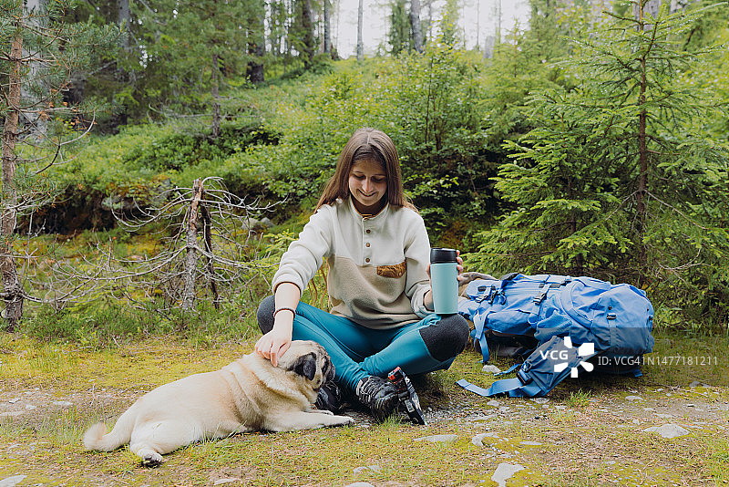 在挪威森林里带着狗放松的快乐女背包客图片素材