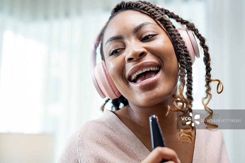 音乐有益于心理健康，调节神经系统。非裔美国女性在家中客厅通过无线耳机听音乐和唱歌。图片素材