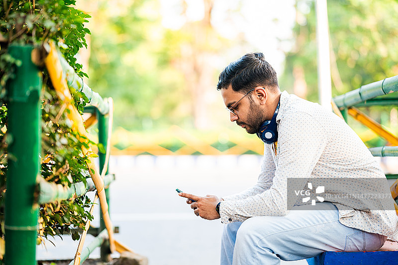 年轻男子坐在公园的椅子上使用智能手机图片素材