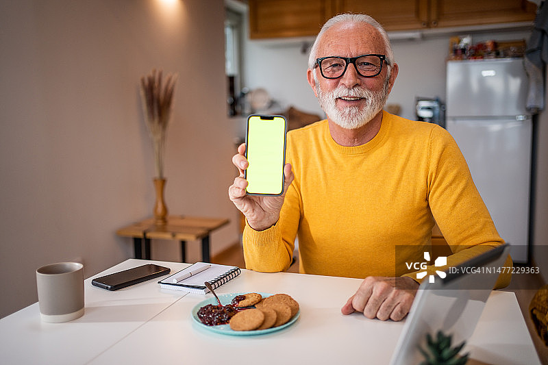 快乐微笑的老年男子展示手机与绿色屏幕图片素材