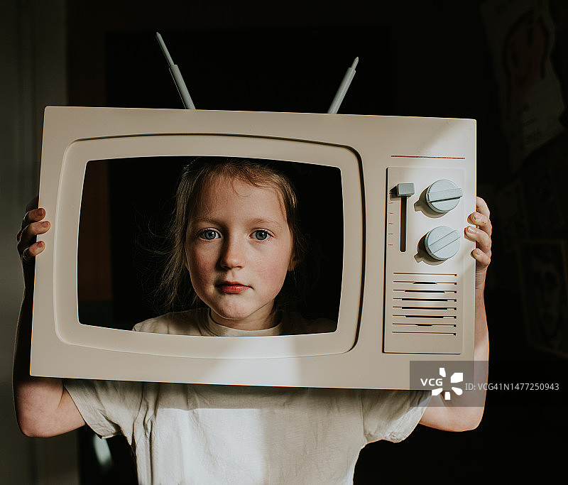 小女孩从玩具电视机后探出头图片素材