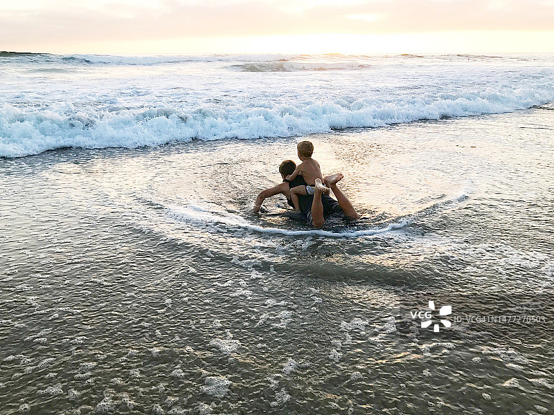 男孩坐在哥哥的趴板上，加州拉古纳海滩图片素材