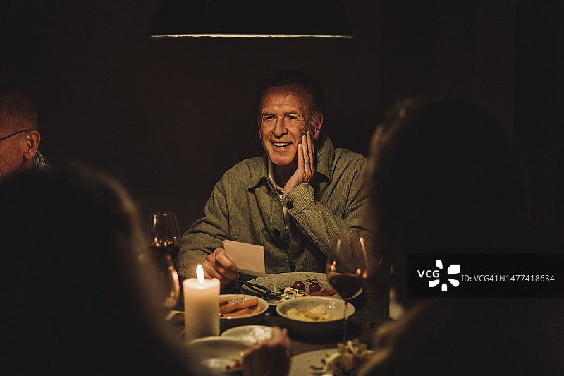 微笑的老年男人在灯光照耀的桌旁享受烛光晚餐派对图片素材