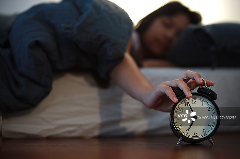 年轻亚洲女孩清晨醒来躺床上关闹钟图片素材