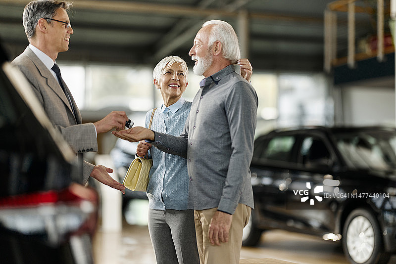 快乐的老年夫妇在展厅里从销售员那里收到新车钥匙图片素材