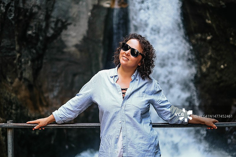 快乐的女人站在美丽的瀑布前微笑（土耳其峡谷之旅）图片素材