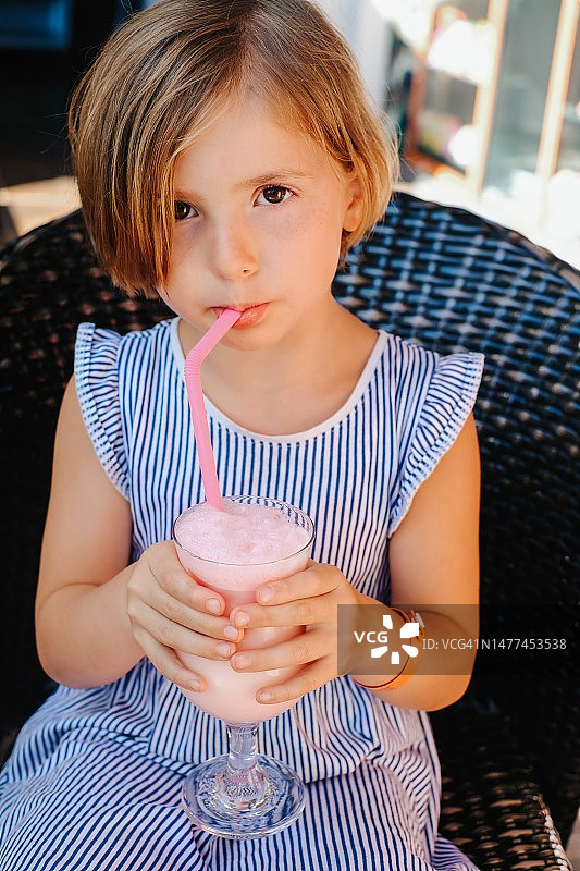 一位5岁短发女孩的肖像：孩子用吸管从大玻璃杯里喝着奶昔，夏天在街上手里拿着大玻璃杯图片素材