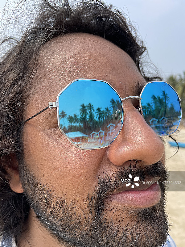 印度男子佩戴反光太阳镜，棕榈树倒影，果阿海滩图片素材