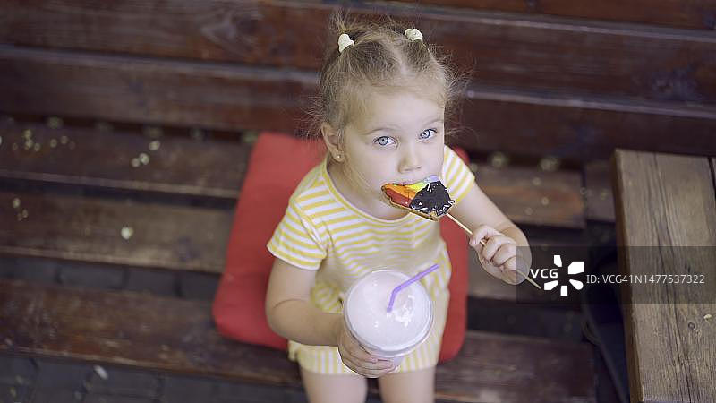 小女孩吃着色彩鲜艳的姜饼，手里拿着奶昔。乌克兰敖德萨，坐在公园长椅上吃饼干喝奶昔的可爱女孩的特写镜头。顶视图图片素材