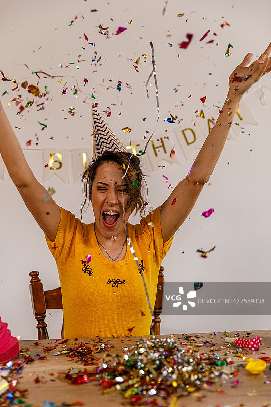 在独自生日庆祝活动中，一位快乐的年轻女子在空中抛洒五彩纸屑的肖像图片素材
