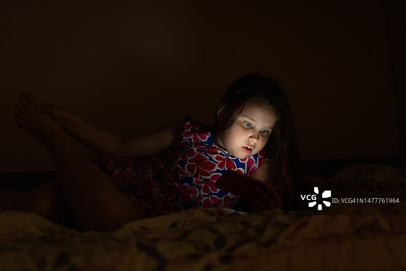 在黑暗中床上用手机的震惊女孩图片素材