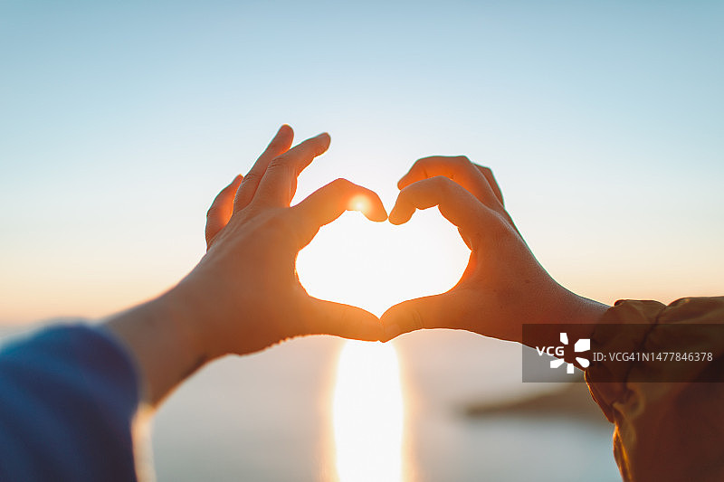 在日落时分的海边用手比心的两个女人图片素材