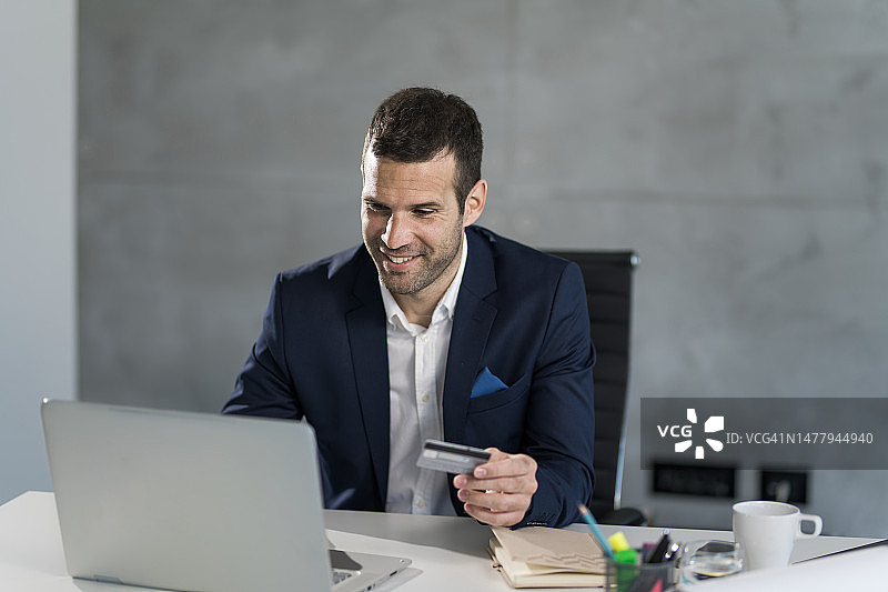 在办公室使用信用卡在线购物的快乐商人图片素材