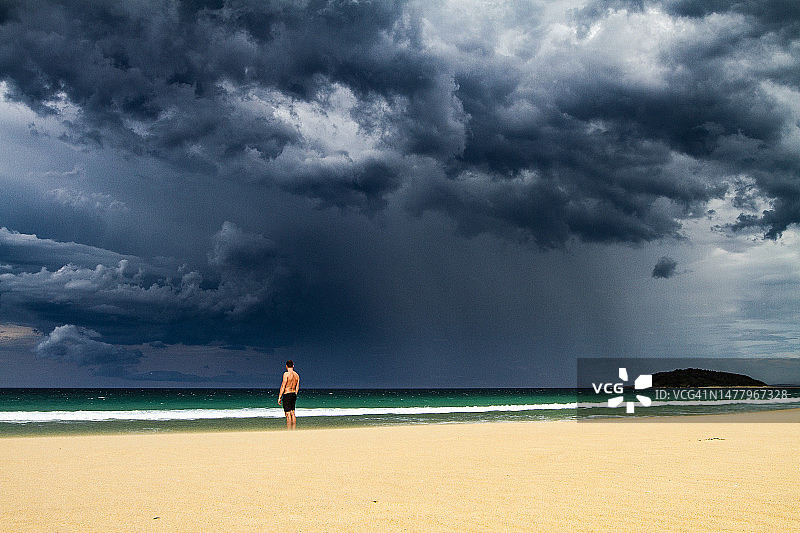 男人站在海滩上，乌云密布，暴风雨即将来临图片素材