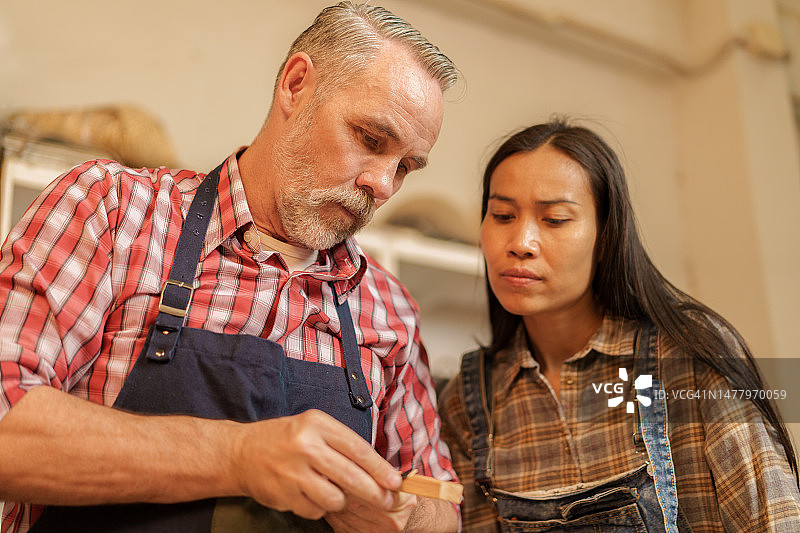 木匠与助手讨论在木工店手工制作家具的木板尺寸图片素材