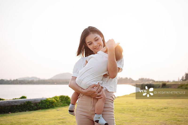 母亲育儿和新生儿生活。 妈妈和男婴在公园日落时玩耍，家庭一起玩乐。 儿童保育，孕产概念。图片素材