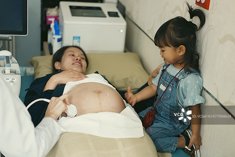 亚洲女婴喜欢看医生用超声波扫描仪为怀孕34周的母亲做检查图片素材