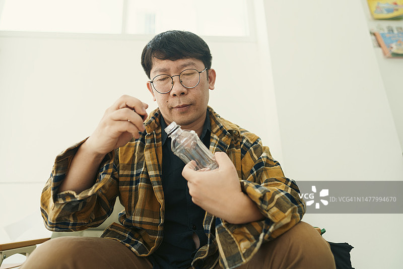亚洲成年人手挤空塑料瓶回收，可持续居家生活图片素材