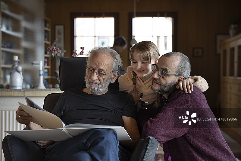 快乐的孩子、父亲和祖父在客厅里一起翻看相册图片素材
