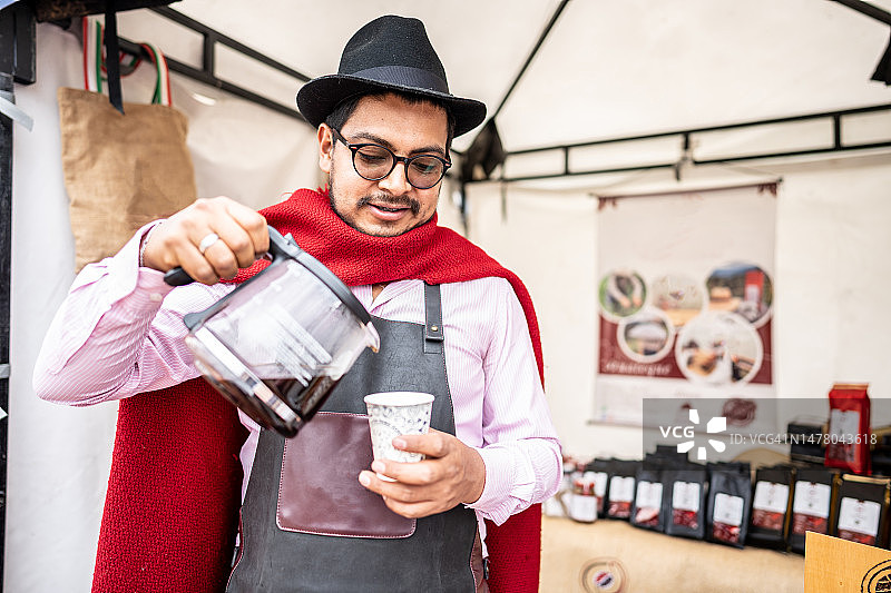 中年男人在市场摊位上用一次性杯子为顾客提供咖啡图片素材