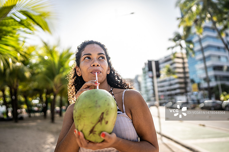 中年妇女在海滩木板路上喝椰子水并四处张望图片素材
