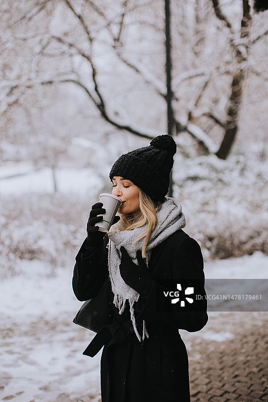 年轻女子穿着暖和的衣服在雪地里享受外卖咖啡图片素材