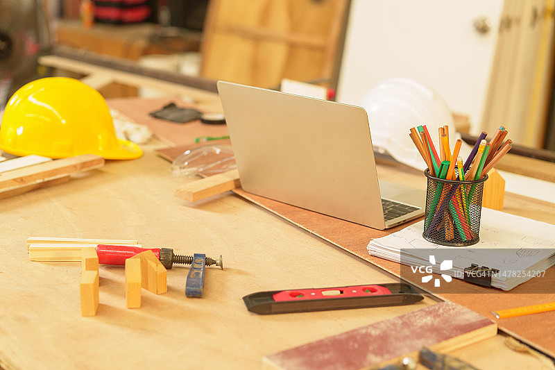 木板上的笔记本电脑、智能手机、写字板、笔、钉子、锤子、刨、锯、卷尺、水平仪、手套、眼镜、咖啡杯、锯末。木工。模型。建筑业务。图片素材
