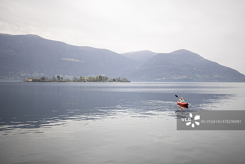阴天在平静的湖上划独木舟的远方人图片素材