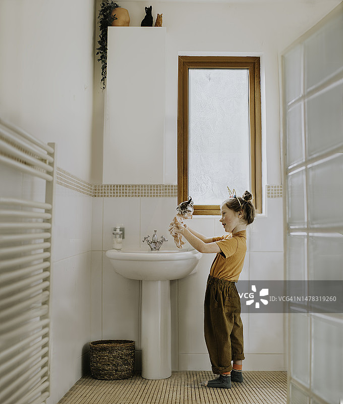 年轻女孩在浴室水槽里清洗橡胶娃娃图片素材