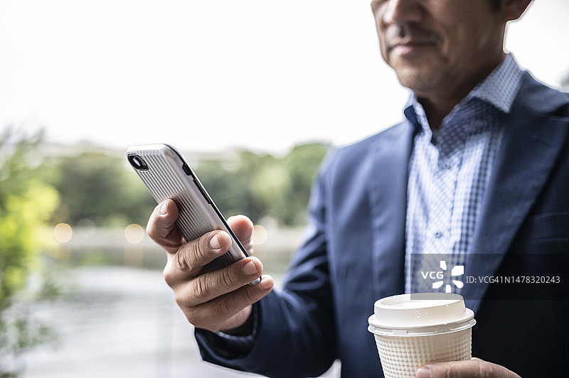 在公园用智能手机发短信的西装革履的商人图片素材