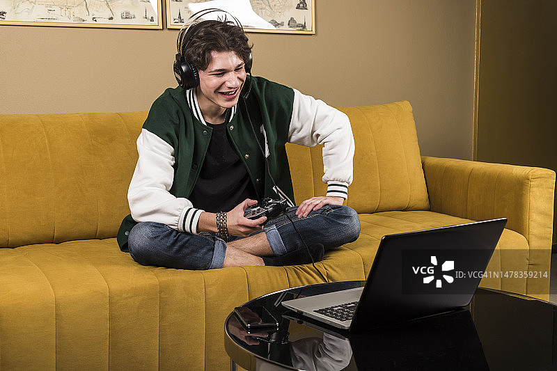 男孩在沙发上戴着耳机用笔记本电脑玩电子游戏图片素材