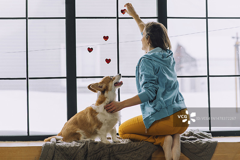 在家中，女人在窗户上贴心形贴纸，狗狗坐在旁边图片素材