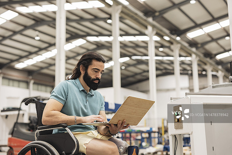 坐在轮椅上的工程师在机器人厂使用笔记本电脑工作图片素材