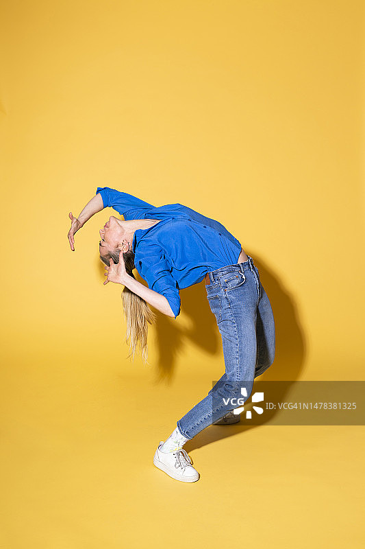 女人在黄色背景下向后弯腰图片素材
