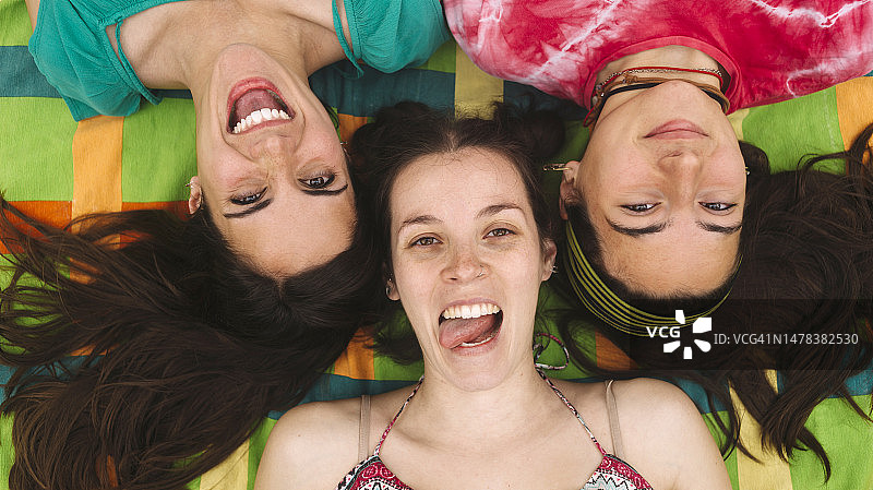 三个年轻女孩在地板上伸展，看着镜头做手势，玩得很开心的俯视图图片素材