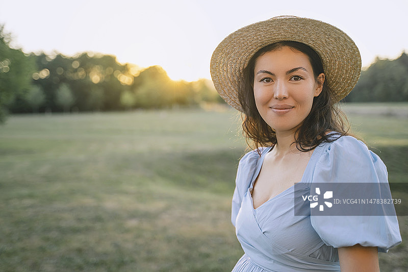 微笑的女人戴着帽子站在日落公园图片素材