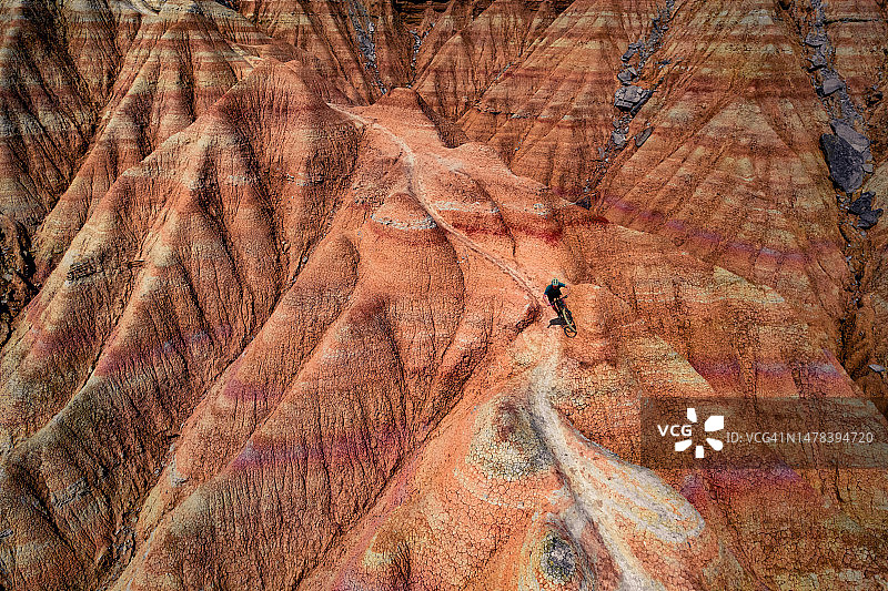 壮丽的航拍：山地自行车手在西班牙巴尔德纳斯雷亚莱斯沙漠荒地的砂岩地层之间的蜿蜒小径上骑行图片素材