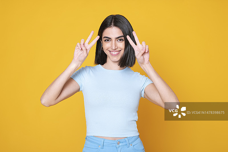 年轻女子在黄色背景前比出和平手势图片素材