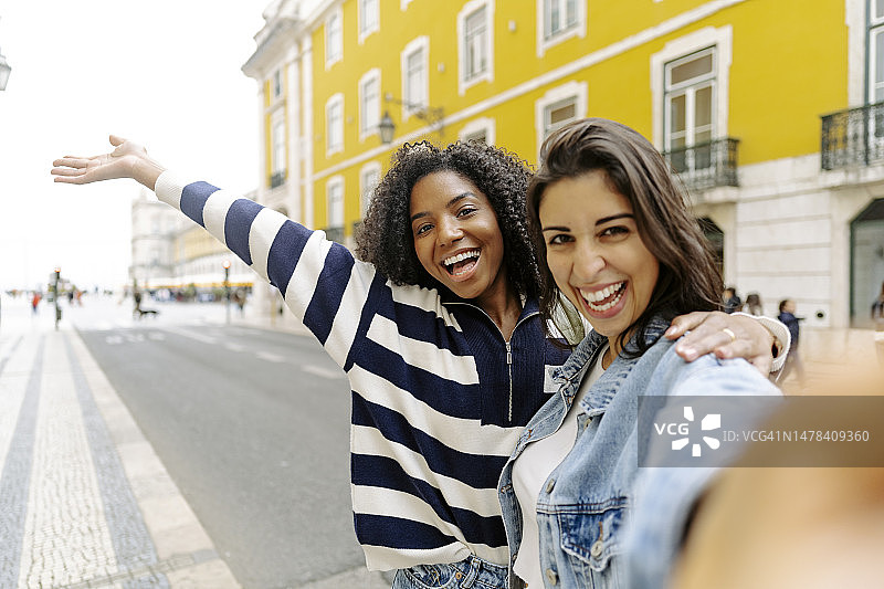 快乐的女人在黄色建筑前的路上与朋友自拍图片素材